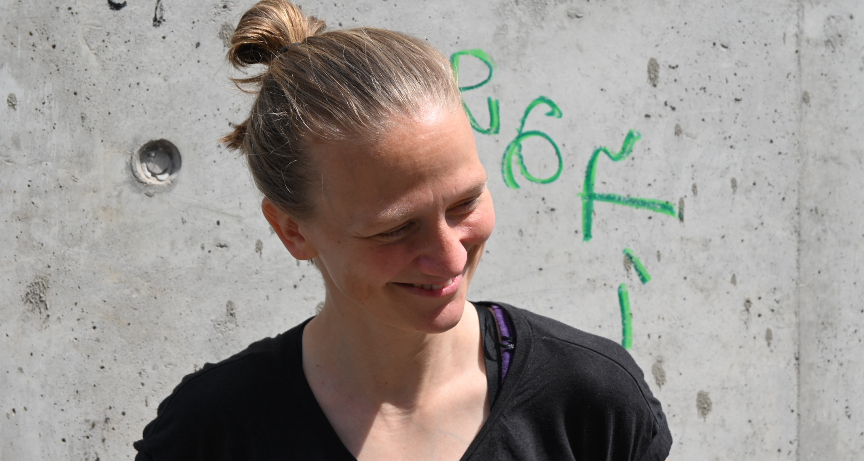 A portrait of myself standing in front of a concrete wall with bright sunlight in my face, smiling.